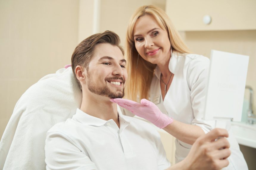 Male beauty clinic patient smiling into handheld mirror